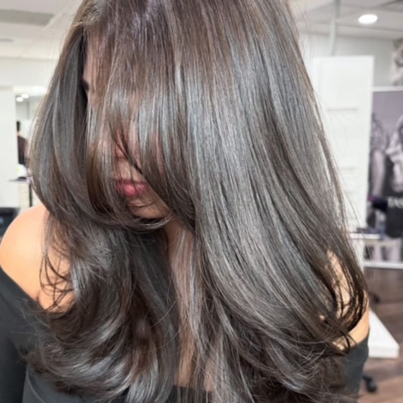 A woman with long, dark hair receiving a haircut at Elavína Salon and Spa in Manchester, NH.