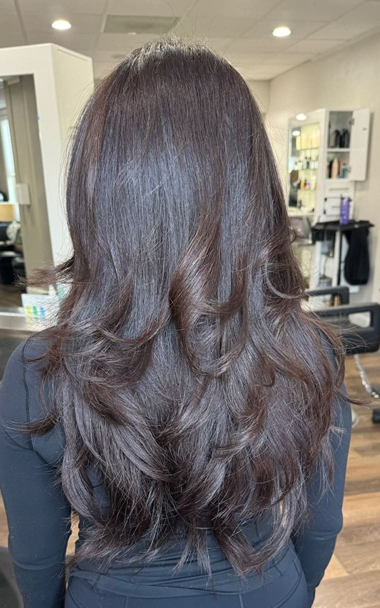 Woman with dark hair showcases salon transformation at Elavína Salon and Spa.