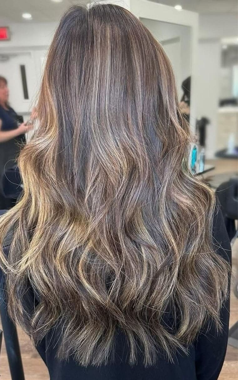 Back view of a woman with long, wavy hair showcasing a hairstyle transformation at Elavína Salon and Spa.